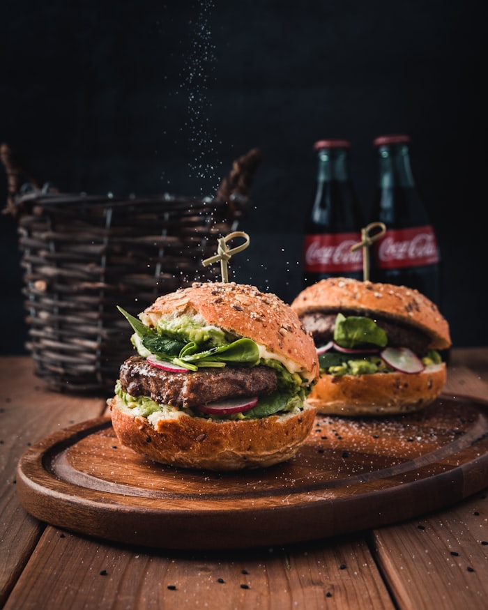 Two burgers with greens on a wooden board